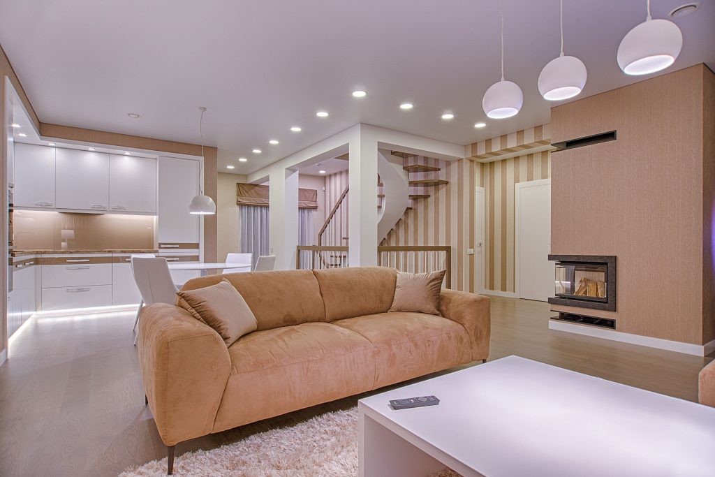 Luxurious living room with modern interior design, featuring beige sofa, fireplace, and open kitchen.